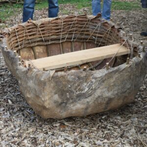 A small, sub-square boat made of a lightweight wooden frame, covered with leather, and with a wooden seat across the middle